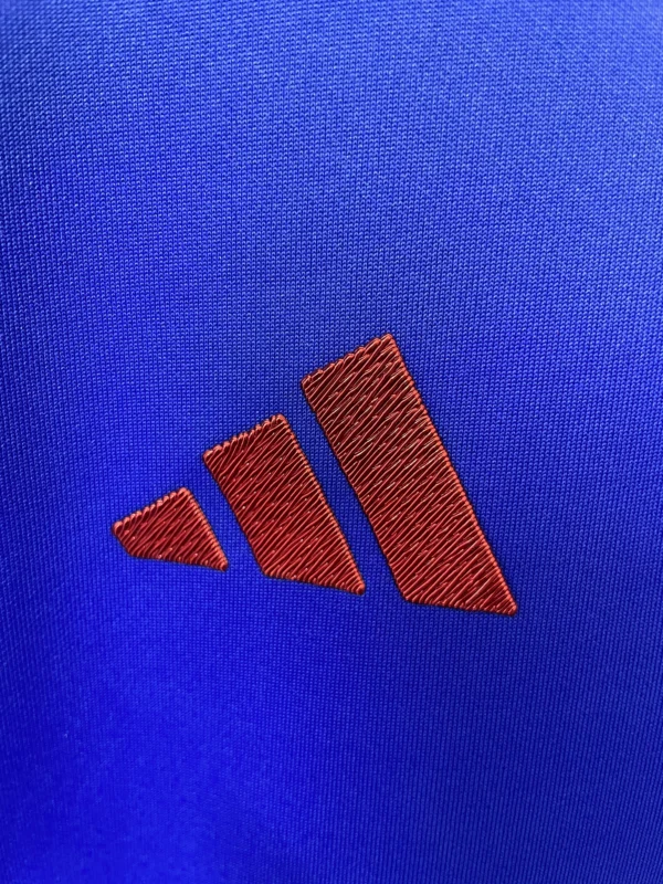 Sportswear logo on blue fabric background. Adidas logo embroidered on athletic clothing or gear.
